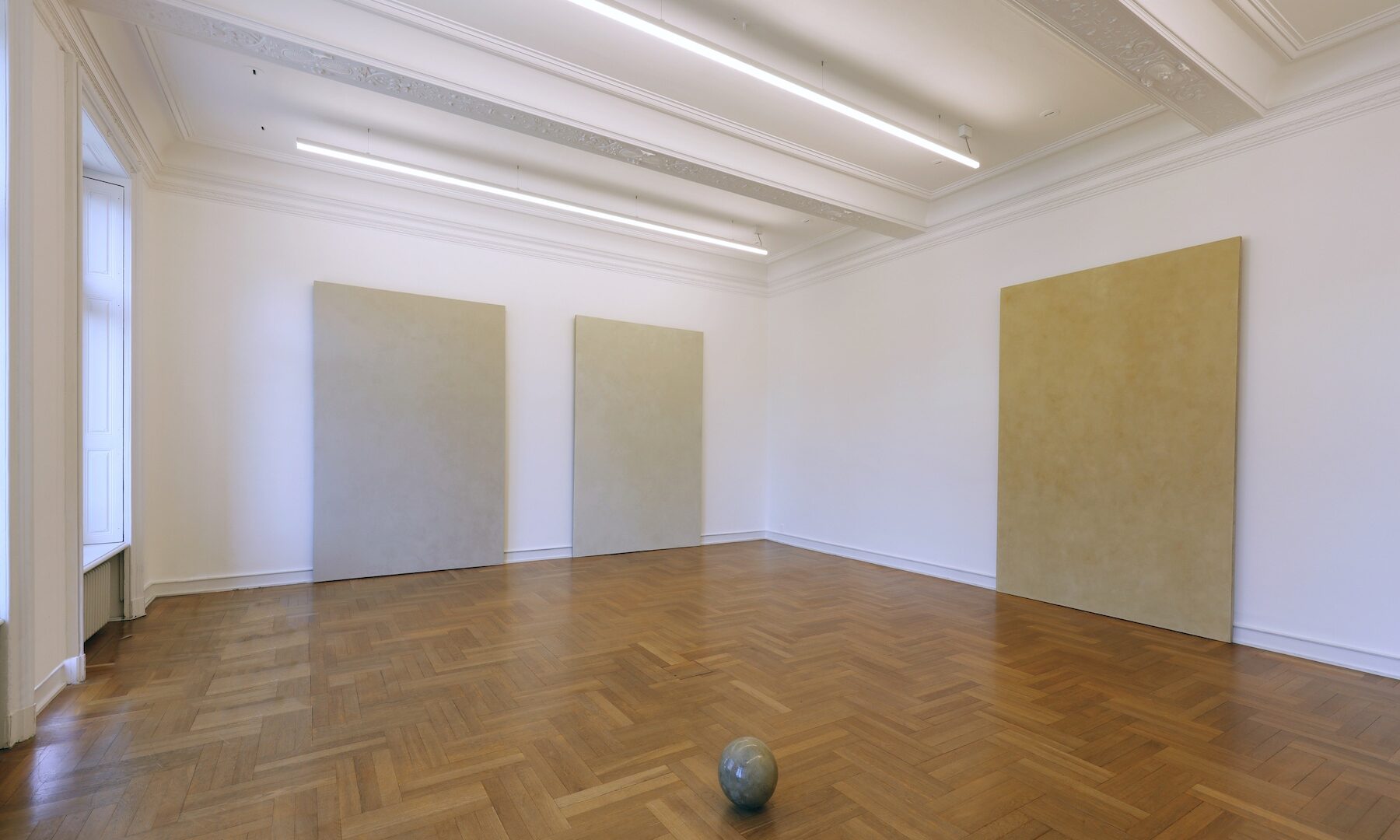 »You begin with the possibilities of the material.« Robert Rauschenberg Die Erfahrung von Prozessen und Veränderungen bildet einen wichtigen Aspekt in der künstlerischen Praxis von Timo Kube - ob als Erlebnis langwieriger Arbeit an einem Werk oder in Form einer sich kontinuierlich verändernden Erscheinung des Werkes selbst. Ausgangspunkt bildet für ihn hierbei die intensive Beschäftigung mit dem von ihm verwendeten Material, das er häufig in Form von Naturmineralien wie Kreide oder Tonerde an öffentlichen Orten und in der Natur findet, so auch im Fall der hier ausgestellten Siegburg-Serie und Sphere. Beiden Werkgruppen liegt dasselbe Material zugrunde: unbe-handelte, ungebrannte Tonerde von Fundorten aus der Umgebung der nordrhein-westfälischen Stadt Siegburg. Ein wesentlicher Unterschied liegt jedoch in der Art ihrer Entstehung. So wurde bei den Arbeiten der Siegburg-Serie die nasse Tonerde zunächst als dünne Schicht auf die liegende Leinwand verrieben und manuell so eingearbeitet, dass der Ton mit dem textilen Gewebe der Leinwand nach und nach eine Verbindung eingeht. Durch den Trockenvorgang entsteht auf der Leinwandoberfläche eine fragile Struktur aus feinen Rissen, kleinen Verdichtungen, Unregelmäßigkeiten und sichtbaren Bearbeitungsspuren, die sich unkontrolliert und selbständig mit der einhergehenden Materialveränderung herausbildet. Der matten, rauen Oberflächentextur der Siegburg-Arbeiten steht die aufpolierte, glatte Oberfläche der Sphere gegenüber. Aus der nassen Tonmasse formte Timo Kube hier zunächst mit den Händen einen Klumpen, den er anschließend mit der einsetzenden Aushärtung des Materials über einen erschöpfend langen Zeitraum von Wochen und Monaten mit einem Teelöffel aus Edelstahl so lange bearbeitete, bis eine nahezu perfekt geometrische Kugel entstand. Die Oberfläche mit den schimmernden Farbnuancen erscheint jetzt makellos glänzend, vielleicht sogar flüchtig, trotzdem wirkt die Sphere nicht schwerelos oder entmaterialisiert. Das einfache Material wird aufgewertet und weckt Assoziationen an Marmor oder Granit ohne dabei die der Tonerde inhärente Fragilität zu verlieren. Sowohl in Siegburg wie auch Sphere zeigt uns Timo Kube jeweils eine Momentaufnahme, einen Erscheinungszustand, der abhängig ist von Raum, Licht und Zeit und der den direkten Dialog mit uns als reflektierende Betrachtende herausfordert. Timo Kube (*1977 in Harsewinkel) lebt und arbeitet in London und Gütersloh. Er studierte u.a. an der Kunstakademie in Münster, wo er Meisterschüler von Ulrich Erben war. Anschließend folgte ein M. A. of Fine Art am Chelsea College of Fine Art & Design in London. Nach zahlreichen nationalen und internationalen Einzel- und Gruppenaus-stellungen erhält Timo Kube mit der Präsentation im Museum Morsbroich seine erste Ausstellungsbeteiligung in einem Museum. http://www.timokube.net https://www.instagram.com/kubetimo/