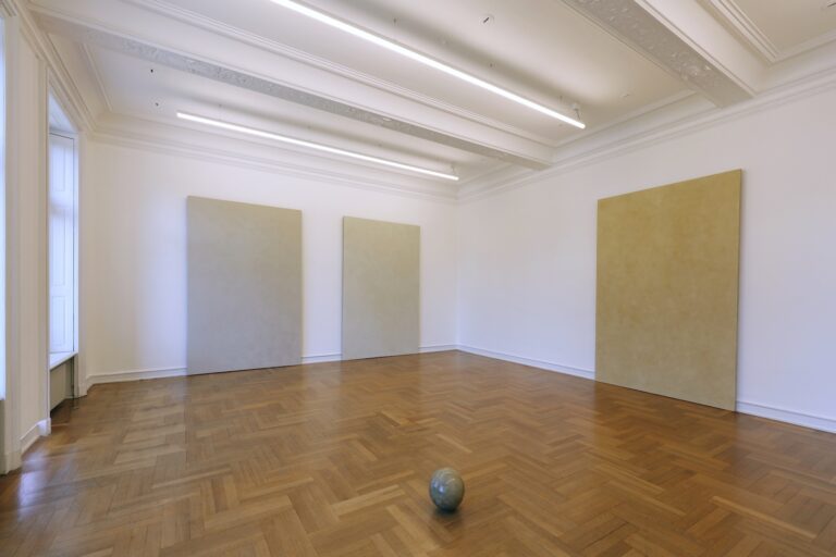 »You begin with the possibilities of the material.« Robert Rauschenberg Die Erfahrung von Prozessen und Veränderungen bildet einen wichtigen Aspekt in der künstlerischen Praxis von Timo Kube - ob als Erlebnis langwieriger Arbeit an einem Werk oder in Form einer sich kontinuierlich verändernden Erscheinung des Werkes selbst. Ausgangspunkt bildet für ihn hierbei die intensive Beschäftigung mit dem von ihm verwendeten Material, das er häufig in Form von Naturmineralien wie Kreide oder Tonerde an öffentlichen Orten und in der Natur findet, so auch im Fall der hier ausgestellten Siegburg-Serie und Sphere. Beiden Werkgruppen liegt dasselbe Material zugrunde: unbe-handelte, ungebrannte Tonerde von Fundorten aus der Umgebung der nordrhein-westfälischen Stadt Siegburg. Ein wesentlicher Unterschied liegt jedoch in der Art ihrer Entstehung. So wurde bei den Arbeiten der Siegburg-Serie die nasse Tonerde zunächst als dünne Schicht auf die liegende Leinwand verrieben und manuell so eingearbeitet, dass der Ton mit dem textilen Gewebe der Leinwand nach und nach eine Verbindung eingeht. Durch den Trockenvorgang entsteht auf der Leinwandoberfläche eine fragile Struktur aus feinen Rissen, kleinen Verdichtungen, Unregelmäßigkeiten und sichtbaren Bearbeitungsspuren, die sich unkontrolliert und selbständig mit der einhergehenden Materialveränderung herausbildet. Der matten, rauen Oberflächentextur der Siegburg-Arbeiten steht die aufpolierte, glatte Oberfläche der Sphere gegenüber. Aus der nassen Tonmasse formte Timo Kube hier zunächst mit den Händen einen Klumpen, den er anschließend mit der einsetzenden Aushärtung des Materials über einen erschöpfend langen Zeitraum von Wochen und Monaten mit einem Teelöffel aus Edelstahl so lange bearbeitete, bis eine nahezu perfekt geometrische Kugel entstand. Die Oberfläche mit den schimmernden Farbnuancen erscheint jetzt makellos glänzend, vielleicht sogar flüchtig, trotzdem wirkt die Sphere nicht schwerelos oder entmaterialisiert. Das einfache Material wird aufgewertet und weckt Assoziationen an Marmor oder Granit ohne dabei die der Tonerde inhärente Fragilität zu verlieren. Sowohl in Siegburg wie auch Sphere zeigt uns Timo Kube jeweils eine Momentaufnahme, einen Erscheinungszustand, der abhängig ist von Raum, Licht und Zeit und der den direkten Dialog mit uns als reflektierende Betrachtende herausfordert. Timo Kube (*1977 in Harsewinkel) lebt und arbeitet in London und Gütersloh. Er studierte u.a. an der Kunstakademie in Münster, wo er Meisterschüler von Ulrich Erben war. Anschließend folgte ein M. A. of Fine Art am Chelsea College of Fine Art & Design in London. Nach zahlreichen nationalen und internationalen Einzel- und Gruppenaus-stellungen erhält Timo Kube mit der Präsentation im Museum Morsbroich seine erste Ausstellungsbeteiligung in einem Museum. http://www.timokube.net https://www.instagram.com/kubetimo/