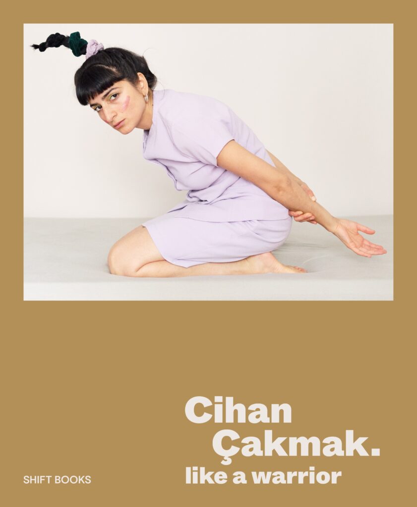 Buchcover „Cihan Çakmak. like a warrior“: eine junge Frau in hellviolettem Anzug kniet auf einem Podest und blickt in die Kamera; darunter der Titel auf ockerfarbenem Grund.